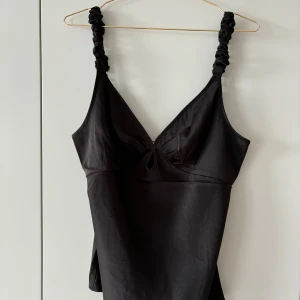 Svart topp från ADOORE - Snygg svart topp från ADOORE med smala axelband som har en twistad design. Toppen har en v-ringning och är perfekt för en stilren look. Aldrig kommit till användning så den är i perfekt skick💕