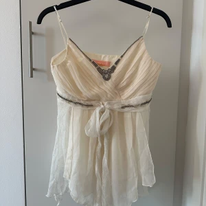 Vit linne med pärldetaljer - Säljer en elegant vit linne med tunna axelband och v-ringad design. Toppen har vackra pärldetaljer vid halsringningen och midjan, samt ett knytband framtill. Den är tillverkad i ett lätt och luftigt material som ger en fin rörelse. Passa som S