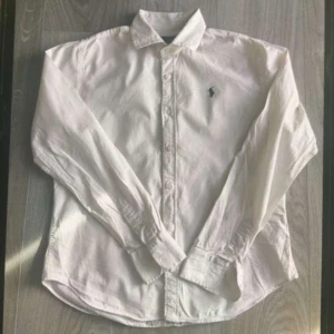 Vit långärmad skjorta med broderad logga Ralph lauren - Klassisk vit skjorta från Ralph Lauren med lång ärm och knappar framtill. Den har en broderad logga på bröstet som ger en stilren touch. Perfekt för en elegant look. Perfekt till sommaren!