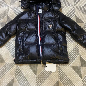 Svart dunjacka från Moncler - Säljer en snygg svart dunjacka från Moncler med en glansig finish. Jackan har en dragkedja i silver och en praktisk bröstficka med Moncler-logga. Perfekt för kyliga dagar med stil! 🖤