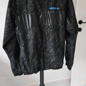 Adidas vindjacka  - Den är en jacka med två sidor, när du vänder den ut och in får du en till jacka  Bild 1 och 2 är den ena sidan  Bild 3 och 4 är jackan när man vänder den ut och in. Storlek L 
