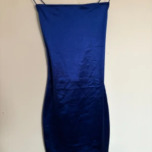 Blå sidenklänning med smala axelband - Elegant blå klänning i siden med smala axelband och öppen rygg. Perfekt för en stilren look.