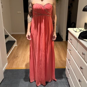 Korallfärgad axelbandslös klänning - Säljer en vacker korallfärgad axelbandslös klänning. Klänningen har snygga strass detaljer med en smickrande passform. Har enbart använt klänningen 1 gång! Perfekt för balen, bröllopet, sittningen, finmiddagen osv! Pris kan diskuteras!💞