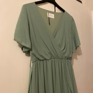 Grön klänning från Sisters Point  - Säljer en elegant grön omlottklänning från Sisters Point. Klänningen har korta ärmar och en v-ringad design med volangdetaljer. Jag har endast haft på mig den 2 gånger. 