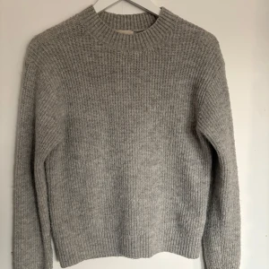 Grå stickad tröja - Säljer en mysig grå stickad tröja med rund hals och långa ärmar. Perfekt för kyliga dagar och enkel att matcha med olika outfits. 