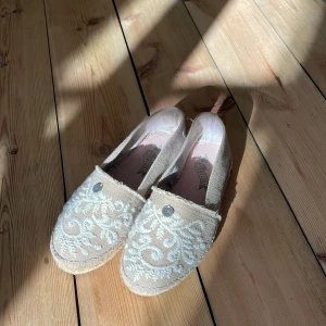 Espadrillos från Odd Molly - Snygga beige espadrillos/sandaler från Odd Molly med vackert vitt broderi på ovansidan. Skorna har en klassisk espadrillos-sula i rep och en liten detalj framtill. Perfekta för en avslappnad sommarlook.