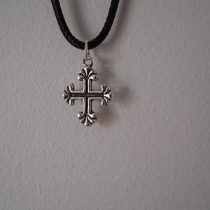 Halsband med korsberlock - Snyggt halsband med en detaljerad korsberlock i silverfärg. Hängsmycket har en elegant design med dekorativa detaljer och hänger på en svart snodd. Perfekt för att ge en stilren touch till din outfit.