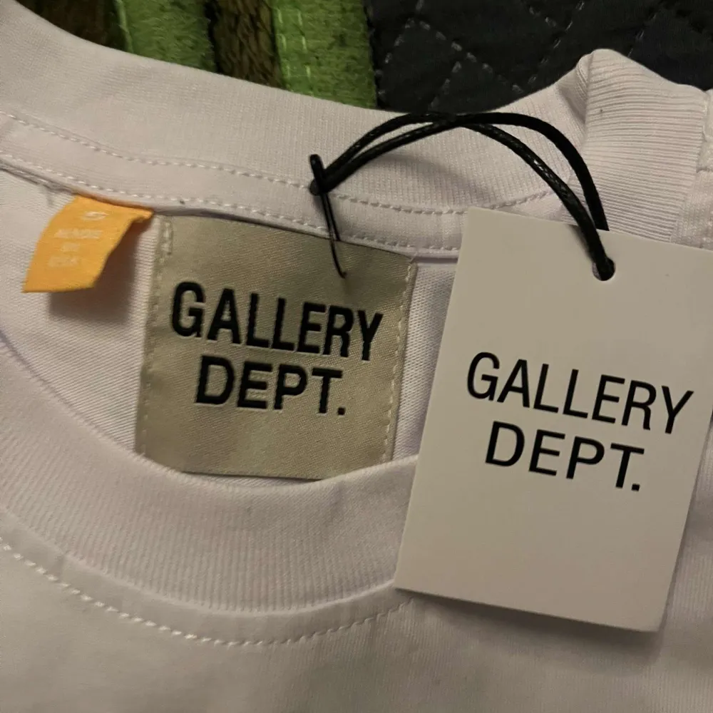 Säljer en stilren vit t-shirt från Gallery Dept. med tryck på bröstet och ryggen. Perfekt för en avslappnad look. T-shirten har korta ärmar och en klassisk passform.. T-paidat.