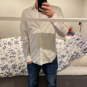 Vit skjorta från Acne - Säljer en stilren vit skjorta från Acne med klassisk krage och knappar framtill. Skjortan har långa ärmar och är perfekt för en elegant look. Passar bra till både jeans och kostymbyxor. Själv är jag 181 ca och den passar perfekt på mig!