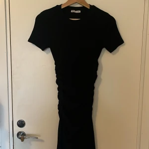 Svart klänning från Zara - Snygg svart klänning från Zara med korta ärmar och en smickrande rynkad detalj på sidan. Perfekt för en stilren look. Klänningen är gjord i ett mjukt och bekvämt material, som formar kroppen på ett magiskt sätt😍i mycket fint skick!