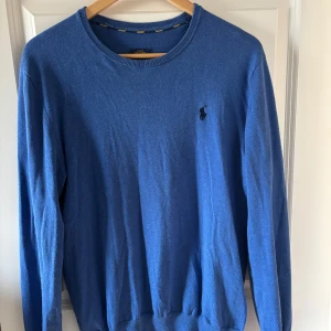 Blå tröja från Ralph Lauren - Säljer en stilren blå tröja från Ralph Lauren i pima bomull. Tröjan har en slim fit passform och långa ärmar. Den är perfekt för våren och sommaren. Hör av er vid frågor!