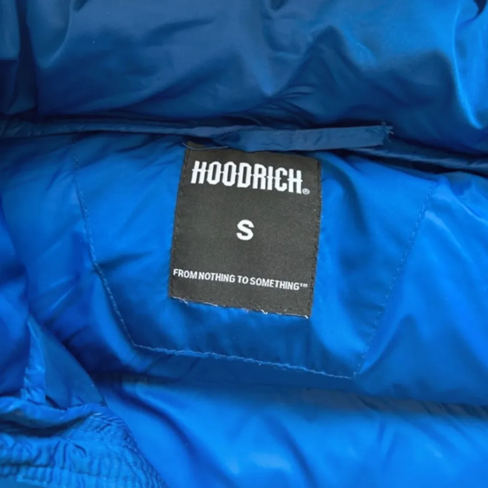 Säljer en blå pufferjacka från Hoodrich med broderad logga på bröstet och ryggen. Jackan har en dragkedja framtill och långa ärmar. Perfekt för kyliga dagar med sin varma och vadderade design.. Takit.