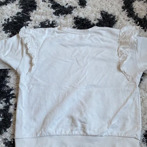 Vit långärmad topp med spetsdetaljer - Säljer en söt vit långärmad topp med spetsdetaljer på axlarna. Perfekt för en stilren och romantisk look. Passar bra till både jeans och kjol. Hör av dig vid intresse! 