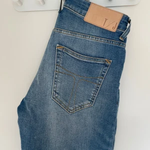 Blå jeans från Tiger of Sweden - Snygga blå jeans från Tiger of Sweden med klassisk femficksdesign och knappgylf. Perfekta för en stilren look. Märkeslappen i läder baktill ger en exklusiv touch. Slim fit med mycket stretch. Väldigt sköna. 28/32