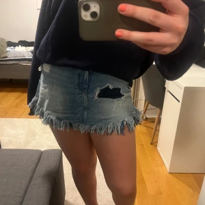 Cool Jeanskjol  - Säljer en cool jeanskjol från TRF Denim med slitna detaljer och fransig kant. Kjolen har en klassisk blå jeansfärg och är perfekt för en avslappnad stil. Den har fickor både fram och bak. Den har inbygda shorts och har högra midja, men går enkelt att dölja med längre tröja.
