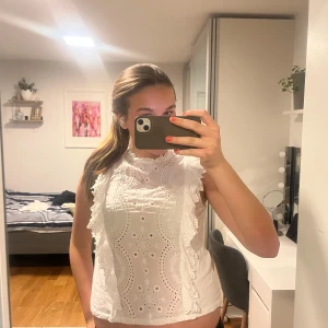 Vit blus med spetsdetaljer - Är en L men sitter en M och S lika bra. Säljer en söt vit blus med vackra spetsdetaljer och broderier. Blusen är ärmlös och har en luftig passform, perfekt för varma dagar. Den har fina volanger längs framsidan som ger en romantisk touch. Passar bra till både jeans och kjol!