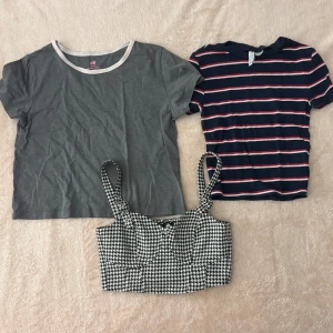 Tre toppar från H&M - Säljer tre olika toppar från H&M. En grå kortärmad t-shirt med vit kant, en randig kortärmad topp i marinblått, vitt och rött, samt en svartvit mönstrad korsettopp med hundtandsmönster och breda axelband. Perfekta för olika tillfällen och stilar!