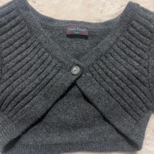 Mörkgrå bolerotopp från Stella Forest - Säljer en stilren mörkgrå bolerotopp från Stella Forest. Den är stickad med ribbade detaljer och har en knapp framtill. Perfekt för att lägga till en extra touch till din outfit. Vet inte vilken stl men är som en s!