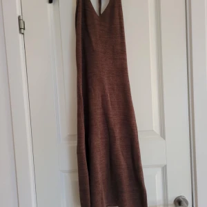 Brun stickad klänning - Säljer en mysig brun stickad klänning med djup v-ringning. Perfekt för en avslappnad stil. Klänningen har en enkel design och är ärmlös, vilket gör den lätt att matcha med olika accessoarer.