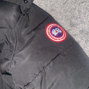  Falkenberg  - Säljer en svart dunjacka från Canada Goose med deras ikoniska märke på ärmen. Jackan har en huva och stängs med både dragkedja och knappar. Perfekt för kalla vinterdagar. 🖤