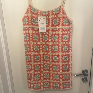 Färgglad virkad klänning från Zara - Säljer en superfin virkad klänning från Zara i härliga färger som orange, grön och beige. Klänningen har ett unikt mönster med fyrkantiga rutor och smala axelband. Perfekt för en somrig look!