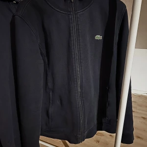 Snygg Lacoste zip upp - Säljer en stilren mörkblå zip upp från Lacoste med dragkedja och det klassiska krokodilmärket på bröstet. Säljer pga att jag vuxit ur den. Pris kan diskuteras.