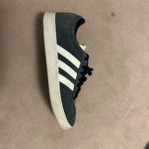Adidas  - Snygga Adidas sneakers i mörkblått med de klassiska tre vita ränderna på sidan. Skorna har snörning och en vit sula. Perfekta för en avslappnad stil.