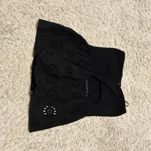 Svart topp med broderade detaljer - Snygg svart topp från Zara med broderade blommönster och en elastisk överdel.Den har ett hål under bysten. Blusen har en kort längd och passar bra till olika tillfällen.