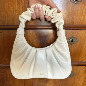 Beige handväska från JW PEI - Snygg beige handväska från JW PEI med ett unikt rynkat handtag. Handväskan är helt oanvänd och nypris ligger på 913kr, säljer för 600kr men priset kan diskuteras. Väskan har en stilren design och är perfekt för att ge din outfit en trendig touch. 
