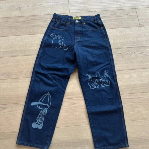 Blå baggy jeans från Butter - Säljer ett par blå baggy jeans från Butter med coola broderade figurer. De har en avslappnad passform och klassisk femficksdesign. Perfekta för en avslappnad stil. Nypris 1200kr