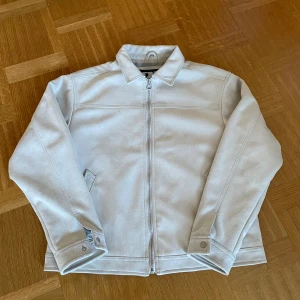 Vit jacka från Pull&Bear - Snygg vit jacka från Pull&Bear med dragkedja och klassisk krage. Jackan har långa ärmar och stilrena fickor framtill. Perfekt för en stilren look.