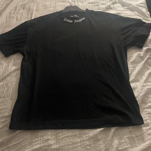 Svart t-shirt från Palm Angels - Snygg svart t-shirt från Palm Angels med deras ikoniska logga tryckt både fram och bak. T-shirten har en klassisk passform och är kortärmad, perfekt för en stilren look.