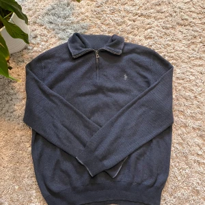 Mörkblå tröja från Ralph Lauren - Säljer en snygg mörkblå tröja från Ralph Lauren med dragkedja och broderad logga på bröstet. Tröjan har långa ärmar och en klassisk krage. Perfekt för en stilren look. Ni ser hålet på sista bilden. Men inga fläckar annars 