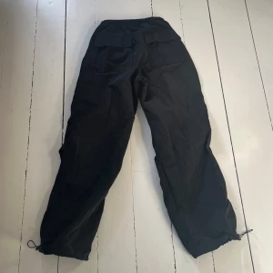 Svarta byxor från Pull&Bear - Svarta byxor (parachute pants) från Pull&Bear med elastisk midja och justerbara dragskor vid benen. Byxorna har en loose passform. Storlek S🖤