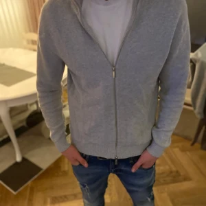 Grå kofta med dragkedja - Säljer en stilren grå kofta med dragkedja. Den har långa ärmar och ribbade muddar vid ärmslut och nederkant. Perfekt för en avslappnad look.