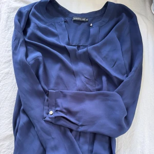 Mörkblå klänning från Stockh  - Säljer en elegant mörkblå klänning från Stockh LM med långa ärmar och rund halsringning. Klänningen har en stilren design med knappdetalj vid ärmslut och mjukt, följsamt tyg.