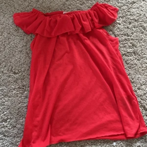 Röd offshoulder topp från H&M - Säljer en röd topp från H&M med offshoulder-modell och volang upptill. Perfekt för dig som gillar en färgstark och trendig stil. Topp är i mjukt material och har en luftig passform.