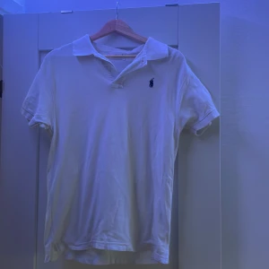 Vit pikétröja från Ralph Lauren - Klassisk vit pikétröja från Ralph Lauren med liten broderad logga på bröstet. Tröjan har korta ärmar och är i storlek S. Har använt en del gånger så därför priset men inga defakter. 