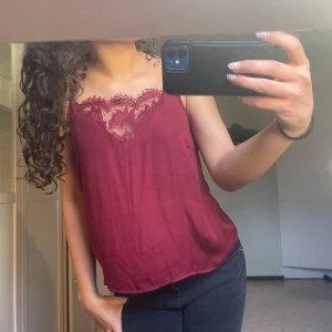 Vinröd linnetopp med spets - Säljer en vinröd linnetopp med vacker spetsdetalj vid urringningen. Toppen har smala axelband och en lös passform, perfekt för varma dagar eller lager på lager. Materialet känns lätt och svalt.