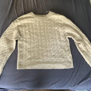 Ljus rosa stickad tröja med kabelmönster - Mysig vit stickad tröja med klassiskt kabelstickat mönster och rund hals. Tröjan har långa ärmar och ribbade muddar vid ärmslut och nederkant. Perfekt för lager-på-lager och passar till det mesta. Säljs i butik för 400 kronor men jag säljer för 150 kronor.
