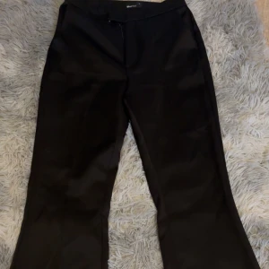 Svarta kostymbyxor från Gina Tricot - Säljer ett par svarta kostymbyxor från Gina Tricot. Byxorna har en klassisk passform med boot cut vid  ben och dragkedja i sidan. Perfekta för en stilren look och passar till många olika outfits.