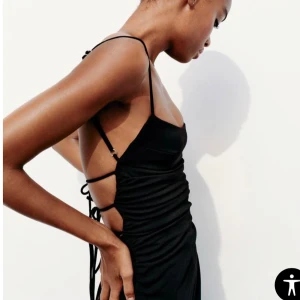 Svart långklänning med öppen rygg och snörning - Säljer en svart långklänning med smala axelband, rynkade detaljer framtill och öppen rygg med flera snörningar. Klänningen har en tight passform men är stretchig och är perfekt för dig som vill ha en stilren och trendig look.