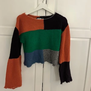 Färgglad stickad tröja från Reclaimed Vintage - Säljer en cool stickad tröja från Reclaimed Vintage med blockmönster i orange, svart, grön, blå och grå. Tröjan är croppad med långa ärmar och har en avslappnad passform. Perfekt för dig som gillar unika plagg!