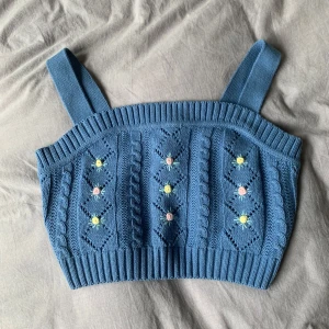 Blå stickad topp med broderade blommor - Supersöt blå stickad topp med breda axelband och små broderade blommor i pastell. Knappt använd. 🌸