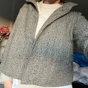 Grå kappa i ullblandning - Säljer en snygg grå kappa med fiskbensmönster och krage. Jackan är i ullblandning och har en rak, lite boxig passform. Perfekt för kyliga dagar och enkel att styla över en stickad tröja. Lite nopprig men inget märkvärdigt 