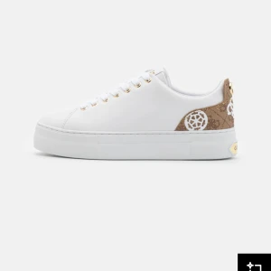 Vita guess sneakers  - Snygga vita sneakers med bruna detaljer och mönster på hälen. Skorna har guldfärgade öljetter och en klassisk rund tå. Perfekta för dig som vill ha en stilren men ändå unik look.