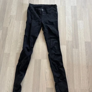 Svarta skinny jeans - Säljer ett par svarta skinny jeans med klassisk femficksdesign och knappgylf. Byxorna har smal passform och är tillverkade i ett stretchigt material som sitter tajt längs benen. Perfekta för en stilren och enkel look. Står ej storlek men gissar på S