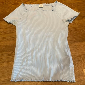 Ljusblå ribbad topp - Säljer en ljusblå ribbad topp från Lindex med korta ärmar och små volangdetaljer vid halsringning 🙏 Toppen har en smal passform och är perfekt för vår och sommar 💕knappt använd