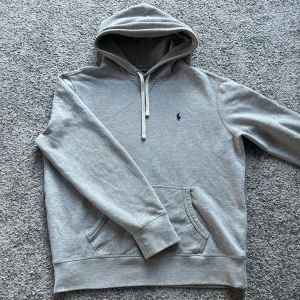 Ralph Lauren hoodie - Säljer en klassisk grå hoodie från Polo Ralph Lauren med broderad logga på bröstet. Tröjan har huva med dragsko och en stor magficka. Perfekt för en avslappnad stil.