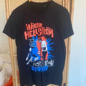 Svart Håkan Hellström t-shirt - Svart t-shirt med färgglatt Håkan Hellström-tryck framtill. Trycket har röda, blå och vita detaljer samt konsertdatum. Klassisk passform och rund hals. Perfekt för dig som gillar musik och vill sticka ut med en cool bandtröja.